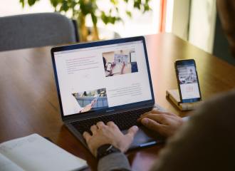 Picture of person at laptop typing with notebook and phone on the desk beside them