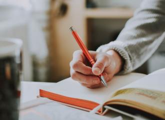 hand holding a pencil, writing on a notebook