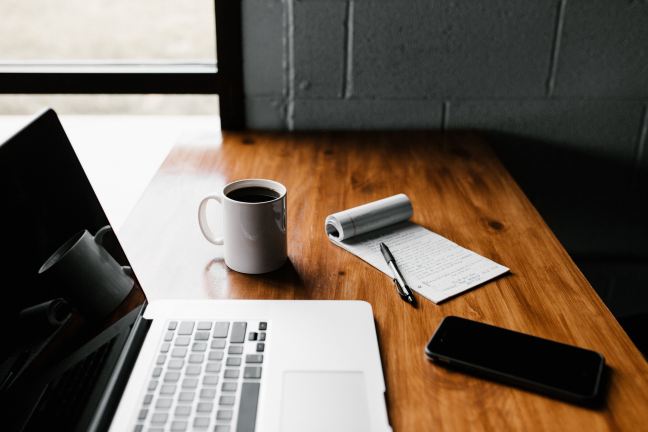 Desk with laptop, notepad and pen and coffee mug