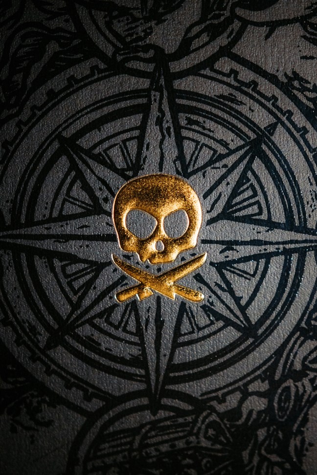 A gold skull and crossbone on a background of black compass